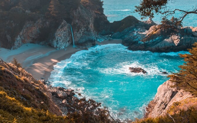 a photo looking down on a rocky bay with bright blue water and trees near the shore